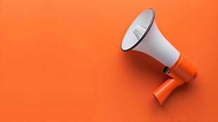 A bright orange megaphone sits on a vivid orange background, symbolizing strong communication and call to action during an event.の素材