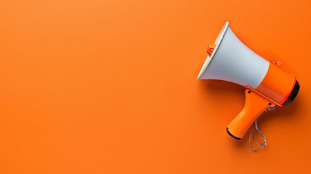 A bright orange megaphone laid on a matching orange background, perfect for making announcements at various gatherings or events.の素材