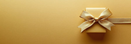 This small golden gift box with a ribbon is placed in the corner on a textured light wrapping paper background, perfect for celebrations.の素材