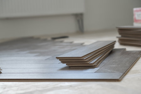 Handyman installing laminate flooring in a residential apartment. Step-by-step process showing tools, underlay, and wooden planksの写真素材