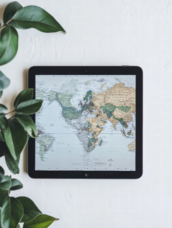 A tablet displays a detailed world map surrounded by lush greenery, offering a perfect space for text or notes on travel plans.の素材