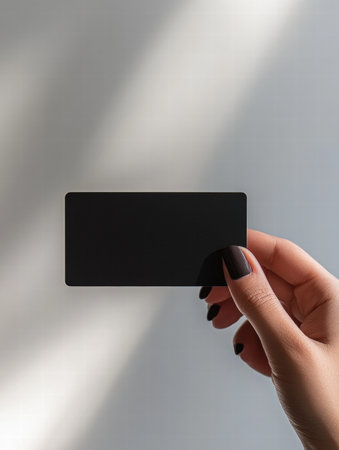 A hand holds a smooth black gift card in a well lit space, providing clear areas for customizable text or design elements.の素材