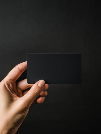 A hand is presenting a modern black gift card against a dark background, providing ample space for customized text and design elements.の素材