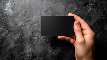 A hand presents a sleek black gift card on a dark, textured surface, offering ample space for personalized text or design elements.の素材