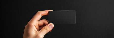 Hand presents a sleek black gift card against a dark background, showing a perfect area for personalized text or design.の素材
