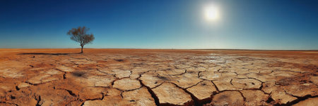 Beneath a relentless blazing sun, a cracked dry lakebed stretches endlessly, punctuated by a solitary tree standing resiliently.の素材