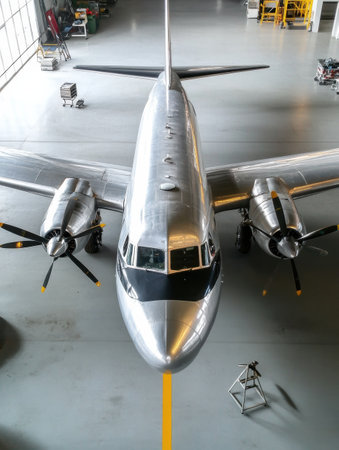 A vintage aircraft is being maintained in a well lit hangar with tools and equipment arranged nearby for efficient repair work.の素材