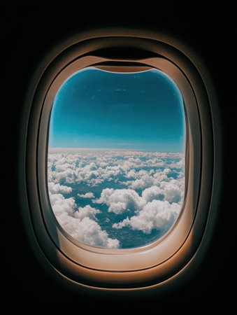 Looking out from the airplane cabin, the wing extends over serene, fluffy clouds with a vibrant blue sky creating a stunning contrast.の素材