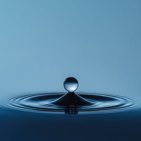 A single water droplet falls into a calm body of blue liquid, creating circular ripples that radiate outward in harmony.の素材