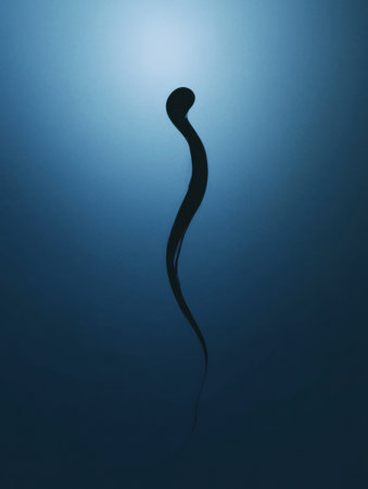 A slender black organism gracefully moves through deep blue water, creating a serene underwater atmosphere during daylight hours.の素材