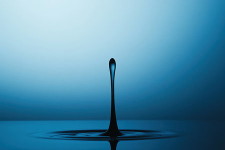 A single droplet falls into still blue water, creating ripples that spread outward under soft, diffused lighting.の素材