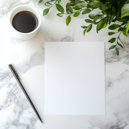 A blank sheet of paper sits beside a shiny pen and a filled coffee cup on a marble tabletop, complemented by lush green leaves nearby.の素材