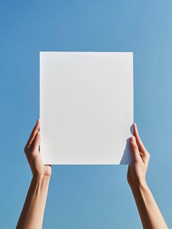 A pair of hands presenting a blank white sheet against an expansive blue sky, demonstrating creativity and expression.の素材
