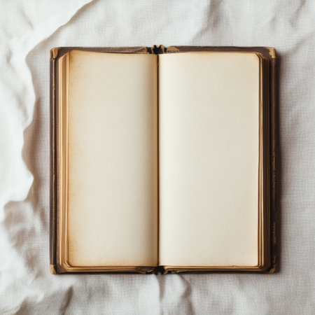 An ancient book with blank pages lies open on soft, textured fabric, illuminated by gentle afternoon light, evoking calmness and introspection.の素材