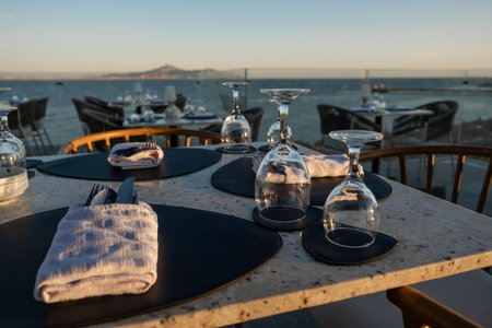 An inviting beachfront restaurant with beautifully arranged tables and a mesmerizing sunset over the oceanの写真素材