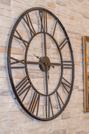A large wall clock featuring Roman numerals hangs elegantly on a textured stone wall, complementing...