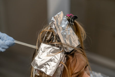 A stylist applies hair dye using foil to separate strands in a salon setting while the client relaxes during an afternoon appointment.の写真素材