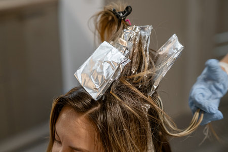 A stylist applies hair color using foil highlights while the client relaxes at a salon during the...