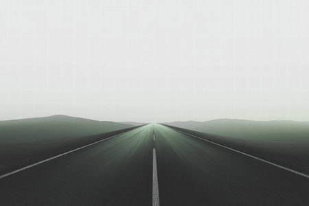 A long, empty road leads into the distance under a foggy sky, surrounded by soft, rolling hills on either side, creating a tranquil setting.の素材