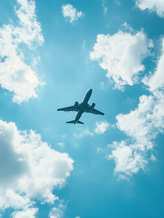 A commercial airplane soars above a vibrant city, surrounded by bright blue skies and fluffy white clouds in the afternoon light.の素材
