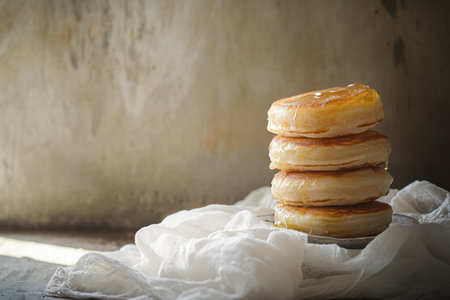 Fluffy pancakes arranged in a stack, glistening with syrup, placed on a soft cloth against a backdrop of warm light.の素材