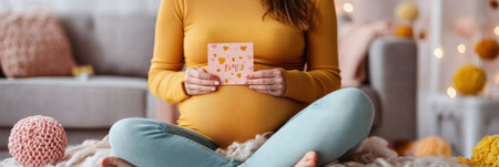 A pregnant woman sits comfortably on a soft blanket, holding a joyful announcement for her upcoming baby, surrounded by warm decor.の素材