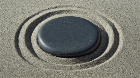 A smooth stone rests in the center of concentric circles in the sand, conveying a sense of stability and inner strength in a peaceful location.の素材