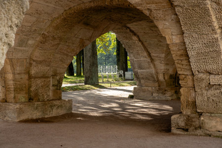 Visitors stroll beneath stone arches in the gardens of the Great Catherine Palace, enjoying the peaceful ambiance and vibrant greenery surrounding the benches.の写真素材
