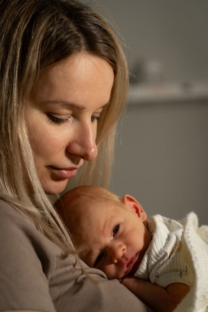 A loving mother holds her baby close in a softly lit room, creating an intimate moment filled with...