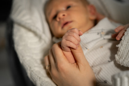 A mother cradles her babys tiny hand in a warm and intimate setting as they share a comforting moment together, reflecting love and tenderness.の写真素材