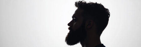 A side profile silhouette of a bearded man showcases sharp facial features and hairstyle. The image has a gradual fade effect blending with a white background.の素材