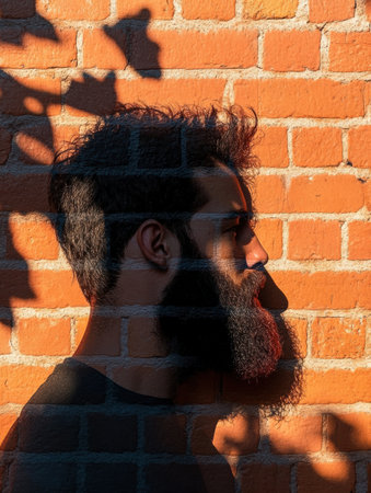 A bearded mans profile casts a dramatic shadow on a textured brick wall, creating an artistic contrast in an urban environment during sunset.の素材