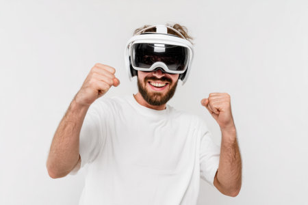 Joyful man with a beard expresses excitement while wearing virtual reality glasses against a flat white background, showcasing modern technology enjoyment.の素材