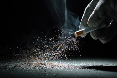 A gloved hand applies pressure to a cigarette, causing ash and smoke to erupt in slow motion against a dark background, capturing the moment.の素材