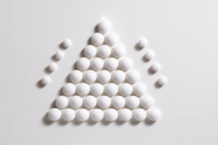 White pills are organized in a precise triangular shape, creating an artistic and minimalist display that emphasizes simplicity and design.の素材