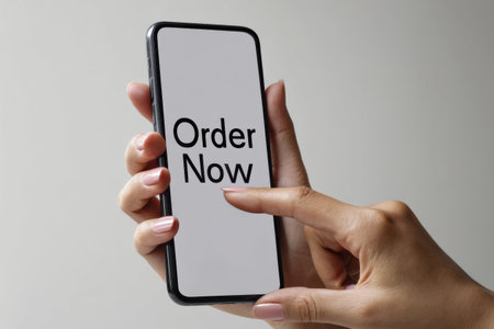A hand taps a smartphones order button, highlighting a clean, minimal design for a convenient online shopping experience.の素材