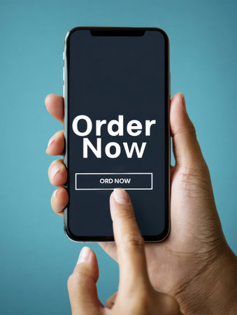 A hand taps the order now button on a smartphone, showcasing a sleek design and minimal style. The backdrop is simple and clean, emphasizing the action.の素材