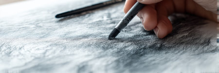 Close-up view captures an artist creating a charcoal drawing on textured white paper, emphasizing the intricate details of the creative process and motion.の素材