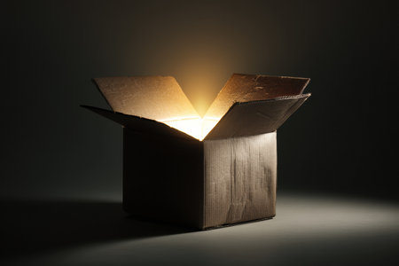 An open cardboard box stands in a dark space, radiating a mysterious, warm glow from within, creating an intriguing atmosphere of curiosity and wonder.の素材