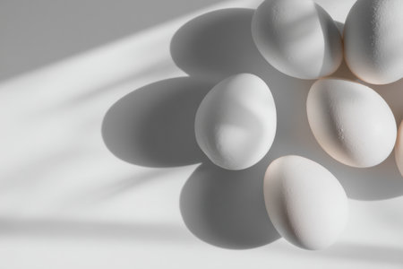 White eggs rest in a corner, their subtle shadows creating visual interest on a clean, bright surface, ideal for branding or display.の素材