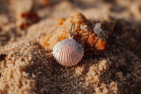 A delicate seashell earring rests on sun-kissed skin surrounded by fine grains of sand, capturing the essence of a beach day.の素材