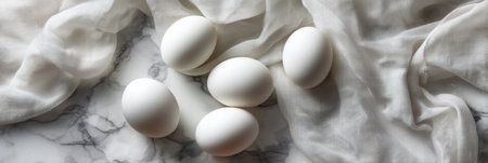 Six white eggs are elegantly arranged on a marble surface, accompanied by soft, flowing fabric, showcasing a stylish and contemporary food presentation.の素材