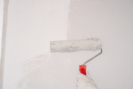 A woman manually paints a wall with a paint roller. Painting the apartment, renovation with white paint.の写真素材