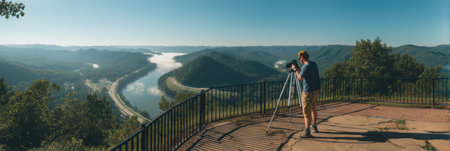 A man prepares his camera tripod at a beautiful overlook, capturing stunning landscapes and distant mountains bathed in morning sunlight.の素材