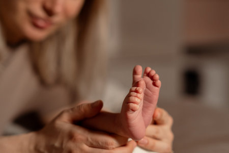 In a warm living room, a mother lovingly cradles her babys small feet, enjoying a special moment of intimacy and connection in the early daylight.の写真素材