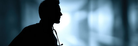 A doctor stands in profile against a softly blurred backdrop, creating a contemplative atmosphere. The stethoscope around the neck adds to the medical theme.の素材