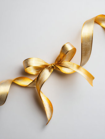 Soft golden ribbon elegantly shaped into a bow on a light background, perfect for suggesting festive occasions, gift wrapping, and creative decoration.の素材