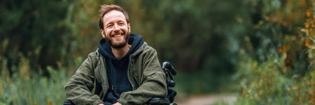 Smiling man in a wheelchair sits outdoors, embracing the beauty of nature with lush greenery in the background on a clear, sunny day.の素材