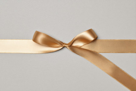 Delicate golden ribbon gently placed on a muted pale surface, serving as an elegant centerpiece for personalized messages or invites.の素材