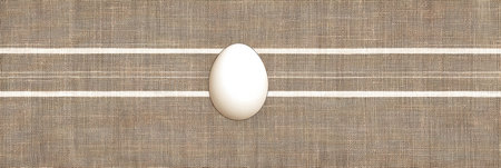 A white egg is centered on a gentle checkered cloth background featuring neutral tones. The overall look creates a serene and minimalist aesthetic.の素材